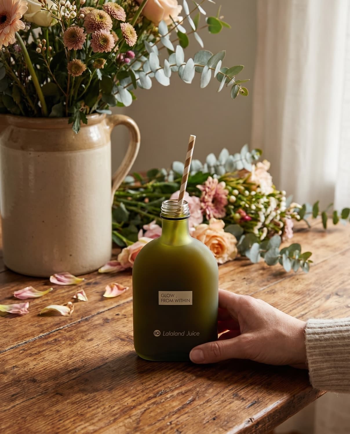 A loose armful of market flowers with a Lalaland bottle in use, a straw through the cap