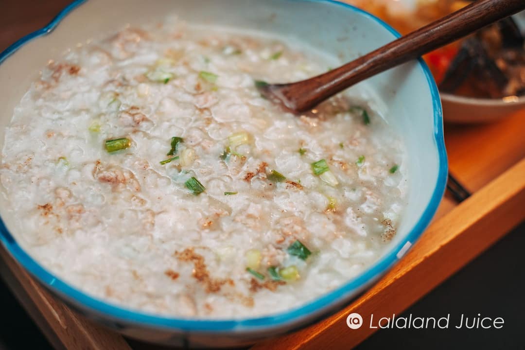 A bowl of soft rice porridge with spring onions, a wooden spoon resting in it — plain, warm, quiet.