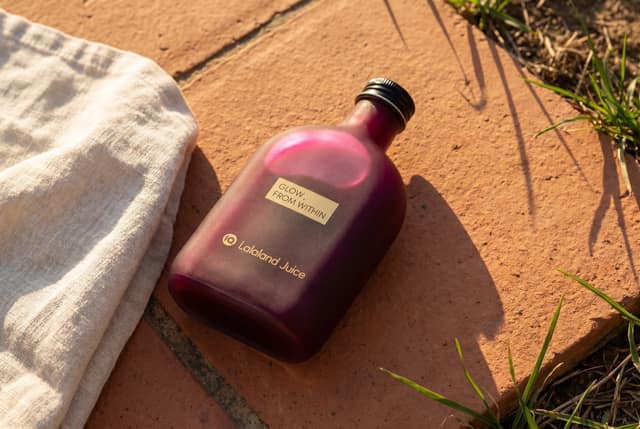 A beetroot Lalaland flask resting on warm terracotta tiles in golden-hour light, linen and grass at the frame's edge.
