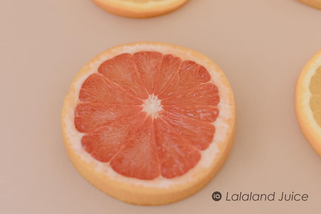 A single ruby grapefruit slice resting on warm sand-coloured paper, the Lalaland Juice mark set quietly within.
