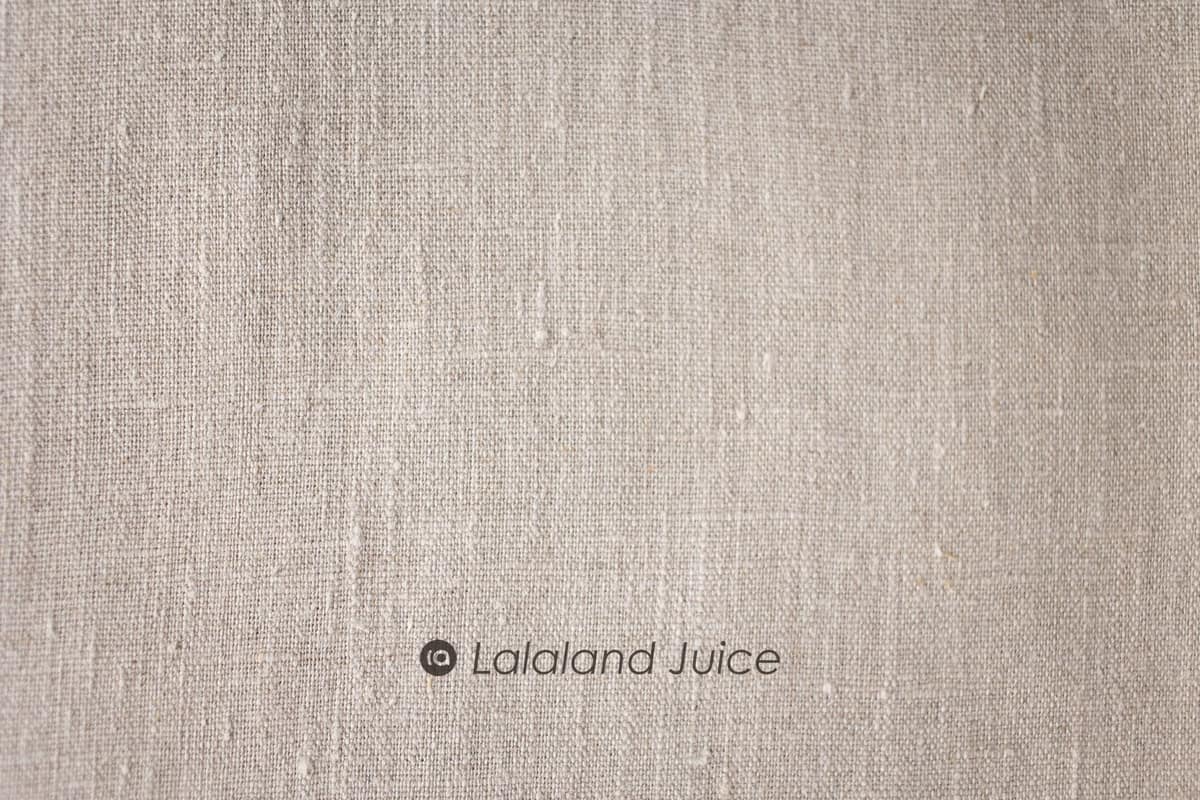 Neutral linen in macro — the weave, the slubs, the quiet — with the Lalaland Juice mark set within.