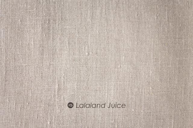 Neutral linen in macro — the weave, the slubs, the quiet — with the Lalaland Juice mark set within.