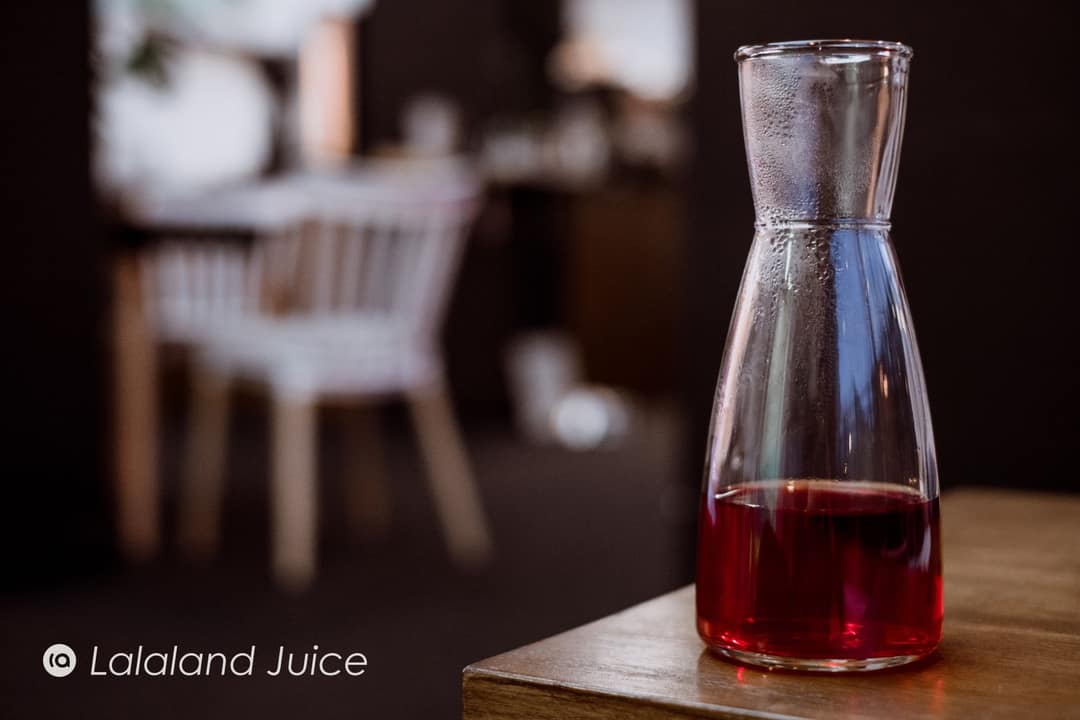 A glass carafe of ruby-red juice beading with cold, set on the corner of a wooden table.